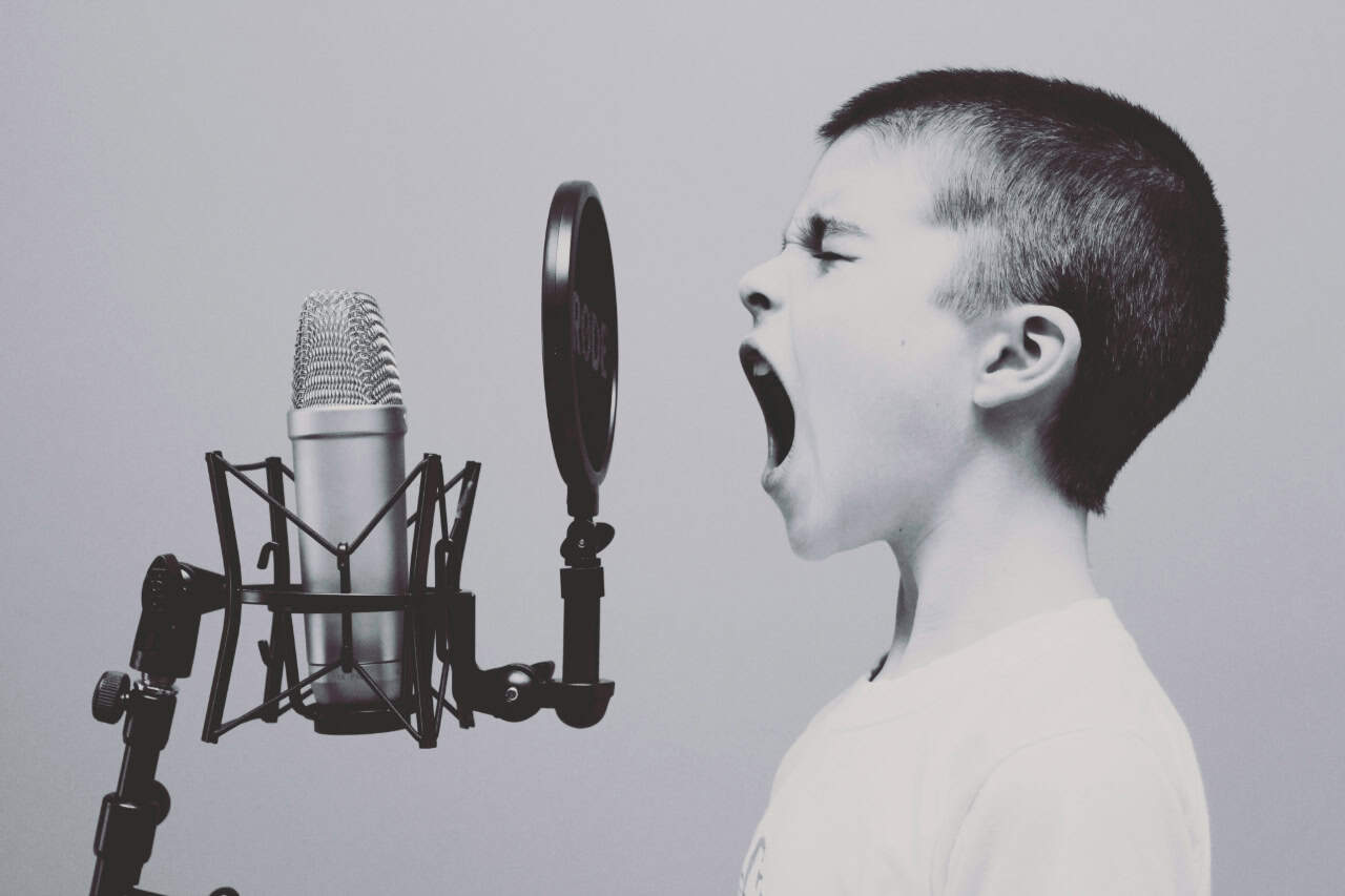 A black and white image of a boy passionately yelling into a microphone, capturing raw emotion and the power of voice, featured on the JourneyWise Studios homepage.