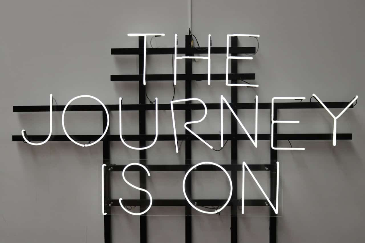 A neon sign hanging on a wall with the text "The journey is on," capturing the essence of ongoing adventure and creativity at JourneyWise Studios.