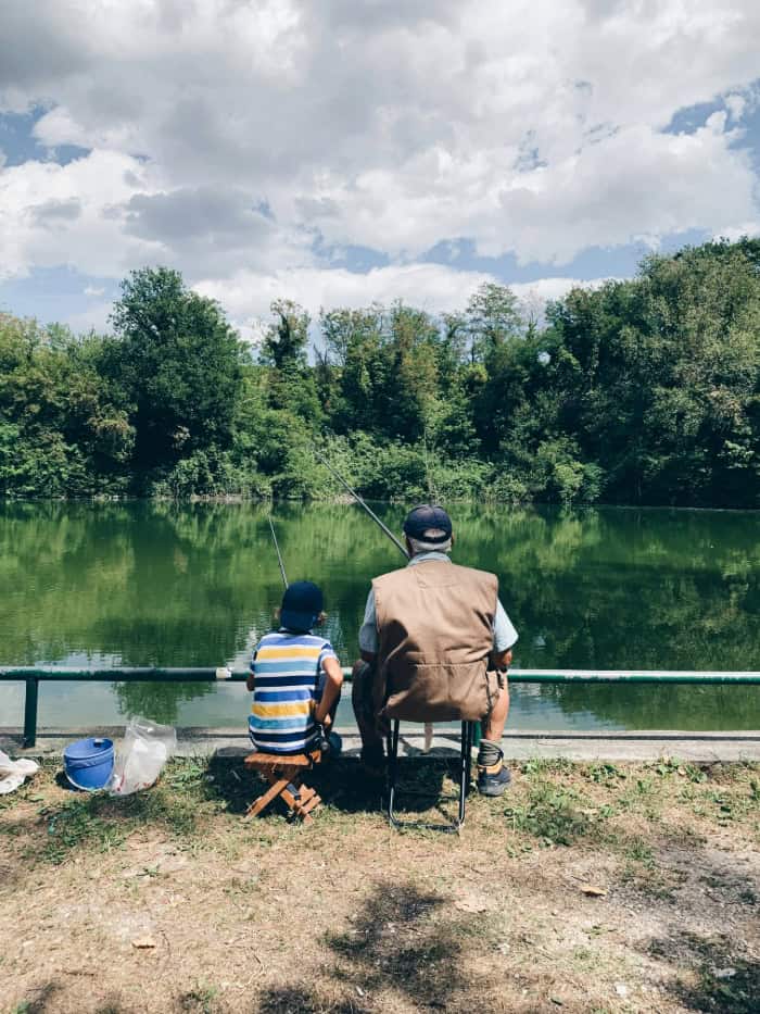 Young boy and grandpa sitting on stools fishing