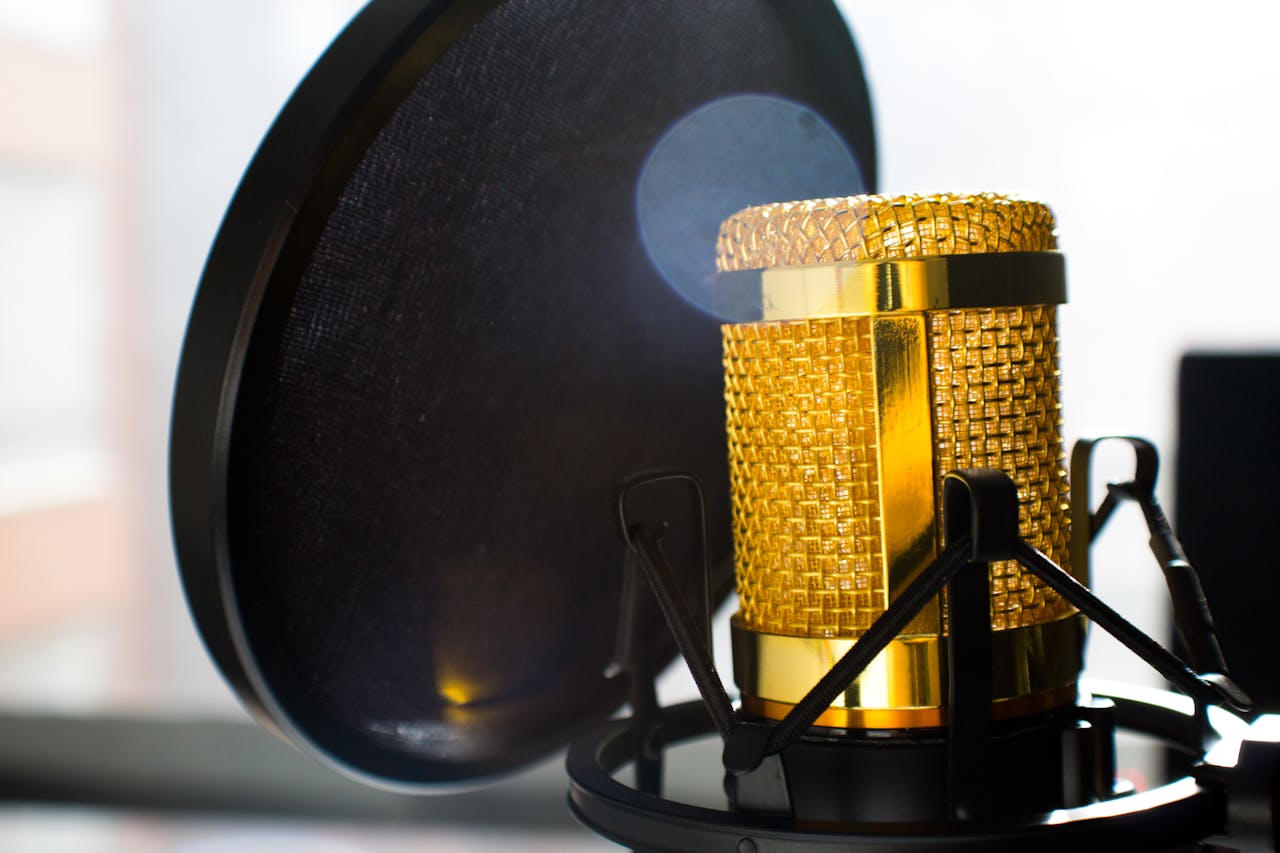 A close-up image of a microphone lit with a gold tone, featuring a pop screen, highlighting the professional audio setup at JourneyWise Studios.